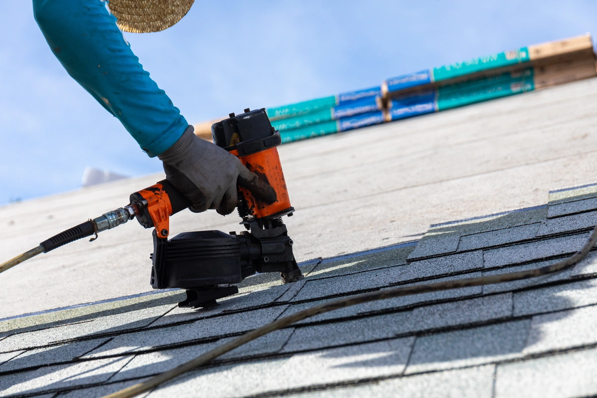 worker installing new shingles using nail gun